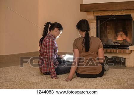 Two women relaxing next to fire and looking at digital tablet View Large Photo Image Stock Image - Two women relaxing next to fire and looking at digital tablet. Fotosearch