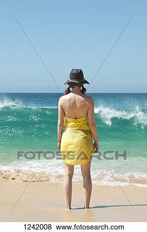 Stock Photo - Woman standing ankle deep in the sand watching the waves. Fotosearch