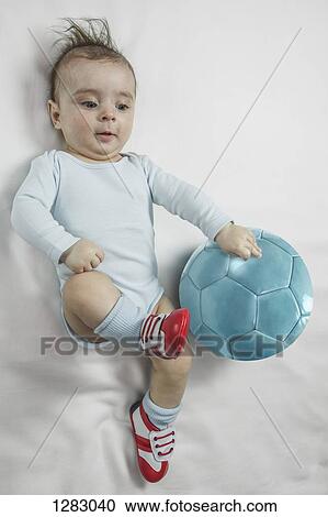 Stock Image - A baby boy wearing baby soccer shoes kicking towards a soccer ball. Fotosearch