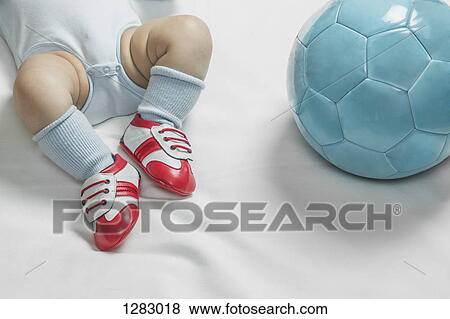 Stock Photo - A baby boy wearing baby soccer shoes lying next to a soccer ball. Fotosearch