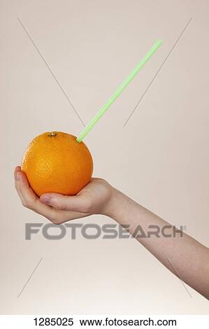 Stock Photography - A girl holding an orange with a drinking straw in it, close-up of arm and hand. Fotosearch