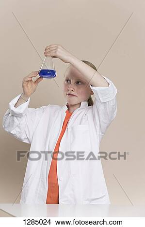 Picture - A girl wearing a lab coat and holding a conical flask with blue liquid in it. Fotosearch