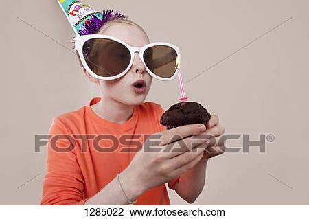 A girl wearing novelty sunglasses and party hat blowing out birthday candle View Large Photo Image Stock Image - A girl wearing novelty sunglasses and party hat blowing out birthday candle. Fotosearch