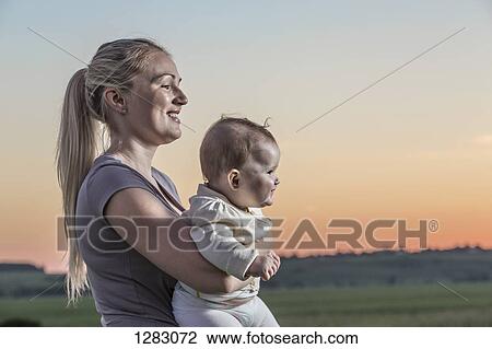 Stock Image - A laughing woman holding her baby in a natural setting. Fotosearch