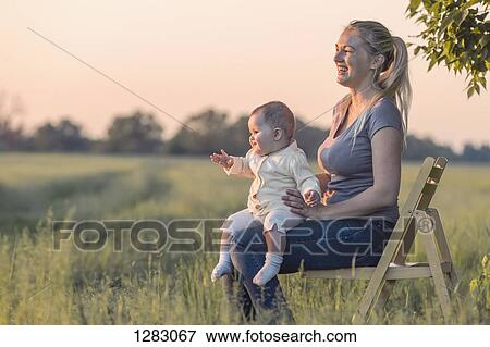 A laughing woman holding her baby while sitting on a chair in a field View Large Photo Image Stock Photo - A laughing woman holding her baby while sitting on a chair in a field. Fotosearch