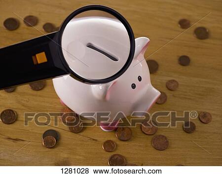 Stock Photo - A magnifying glass magnifying the slot on a piggy bank, coins around it. Fotosearch