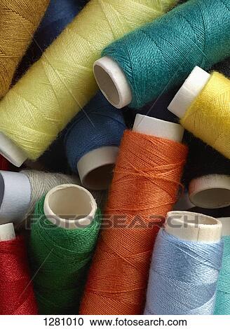 Stock Image - A pile of different colored spools of thread, close-up, full frame. Fotosearch