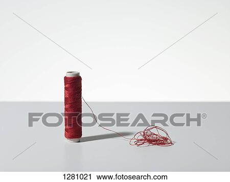 Stock Image - A spool of red thread with a pile of tangled thread. Fotosearch