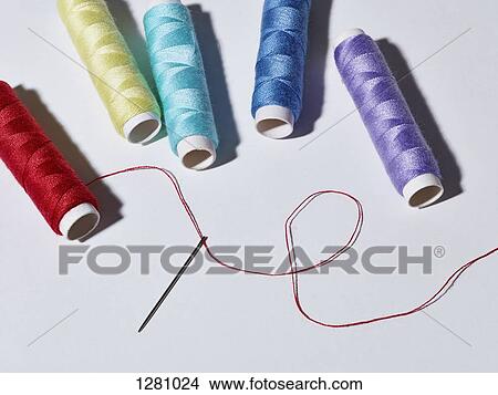 A threaded needle lying below five spools of different colored thread View Large Photo Image Picture - A threaded needle lying below five spools of different colored thread. Fotosearch