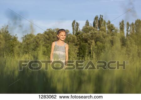 Stock Image - A young cheerful girl standing in a field looking at the view. Fotosearch