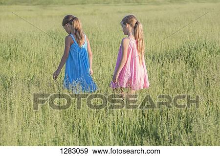 A young girl following her sister, walking through a sunny field View Large Photo Image Stock Photo - A young girl following her sister, walking through a sunny field. Fotosearch