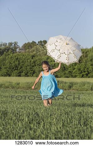 A young girl holding an umbrella up while running through a field in summer View Large Photo Image Stock Image - A young girl holding an umbrella up while running through a field in summer. Fotosearch