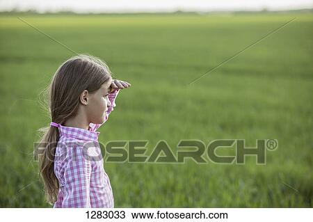 A young girl standing in a field, shielding her eyes and looking at view View Large Photo Image Stock Image - A young girl standing in a field, shielding her eyes and looking at view. Fotosearch