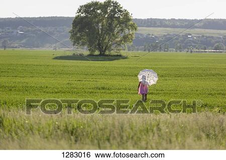 Stock Photograph - A young girl walking through a field using an umbrella as protection against the sun. Fotosearch