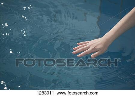 Stock Image - A young girl's hand rippling the water in a swimming pool. Fotosearch