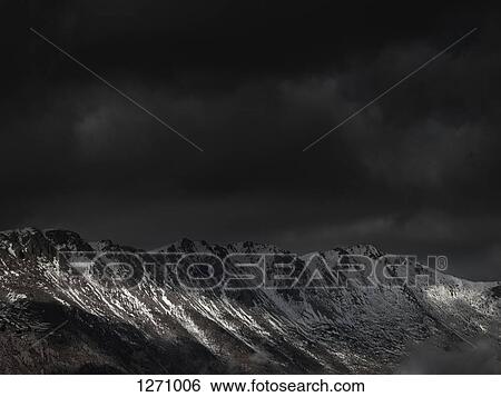 Stock Photograph - An ominous sky with some sunlight breaking through over a mountain range. Fotosearch