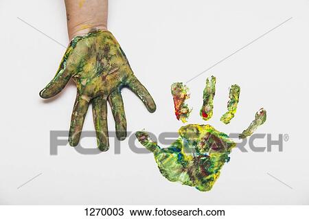 Stock Image - Child with colorful painted hand beside her hand print on paper. Fotosearch