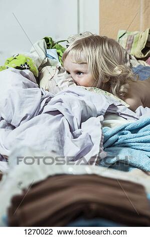Stock Image - Girl on bed peeking over bed clothes. Fotosearch