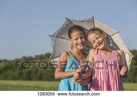 Stock Photography - Laughing twin sisters standing in a field under an umbrella. Fotosearch