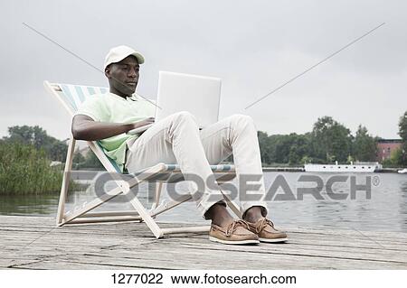 Man relaxing on deckchair with laptop by lake View Large Photo Image Stock Image - Man relaxing on deckchair with laptop by lake. Fotosearch