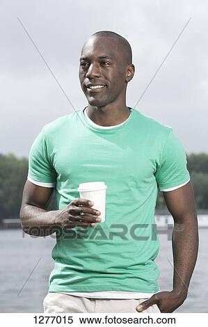 Stock Photography - Man relaxing with disposable coffee cup by lake. Fotosearch