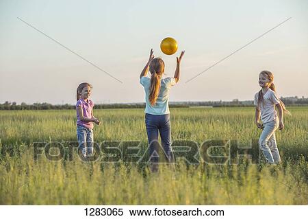 Stock Photography - Three young girls playing catch in a sunny field in summer. Fotosearch