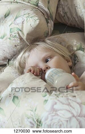 Stock Image - Tired girl on bed drinking from milk bottle. Fotosearch