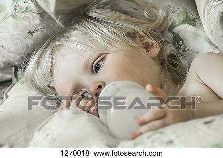 Tired girl on bed drinking from milk bottle View Large Photo Image Stock Photo - Tired girl on bed drinking from milk bottle. Fotosearch