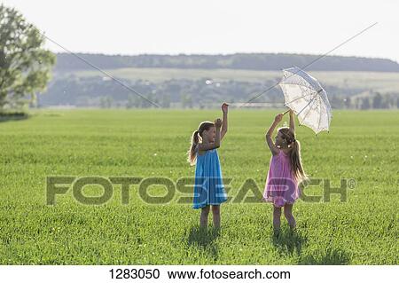 Stock Image - Twin sisters having fun while playing in sunny field. Fotosearch