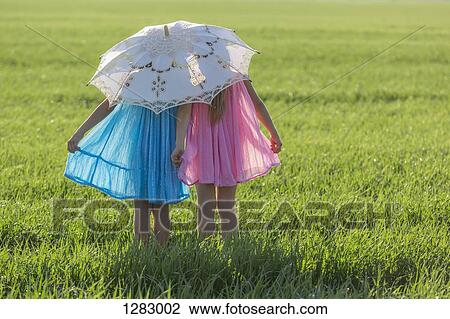 Stock Image - Twin sisters standing in a sunny field under an umbrella. Fotosearch