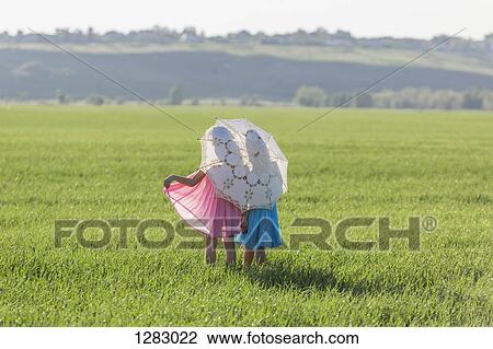 Twin sisters standing in a sunny field under an umbrella View Large Photo Image Stock Image - Twin sisters standing in a sunny field under an umbrella. Fotosearch
