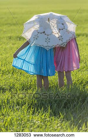 Stock Image - Twin sisters standing in a sunny field under an umbrella. Fotosearch