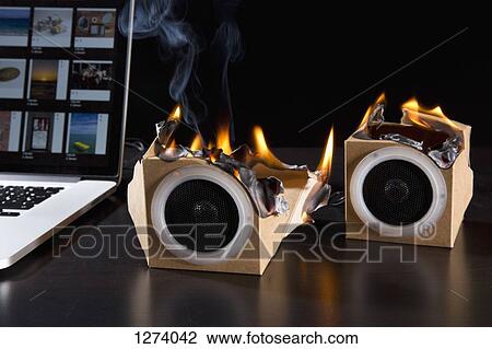 Stock Image - Two eco friendly cardboard audio speakers on fire next to a laptop. Fotosearch