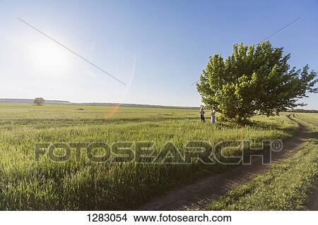 Picture - Two mothers holding their babies while standing in a field. Fotosearch