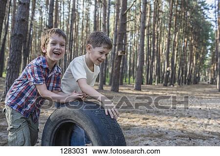 Two young boys pushing a tire in a wooded area View Large Photo Image Stock Image - Two young boys pushing a tire in a wooded area. Fotosearch