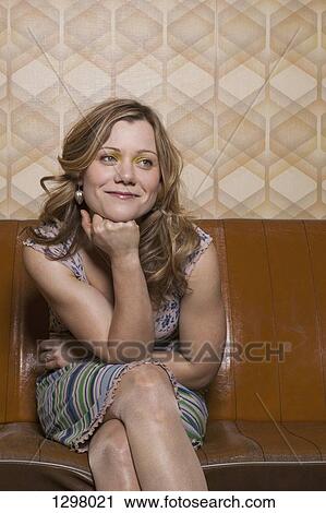 Stock Image - A smiling woman sitting on sofa, looking away. Fotosearch