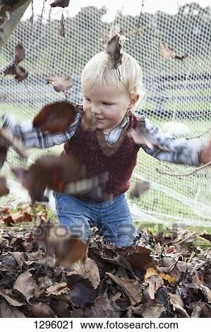 Stock Image - Baby boy throwing dry leaves. Fotosearch
