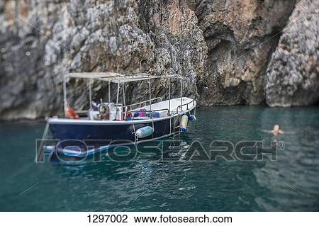 Boat floating on water by rock formation View Large Photo Image Stock Image - Boat floating on water by rock formation. Fotosearch