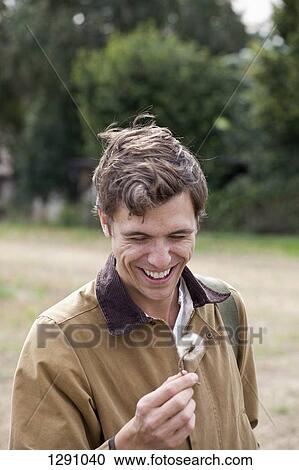 Stock Image - Man holding dandelion flower, smiling. Fotosearch