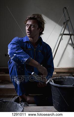 Man wearing workwear sitting with paint bucket View Large Photo Image Stock Image - Man wearing workwear sitting with paint bucket. Fotosearch