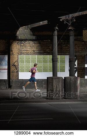 Mid adult man jogging on footpath View Large Photo Image Picture - Mid adult man jogging on footpath. Fotosearch