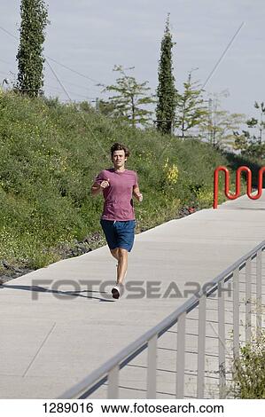 Mid adult man jogging on footpath View Large Photo Image Stock Photograph - Mid adult man jogging on footpath. Fotosearch