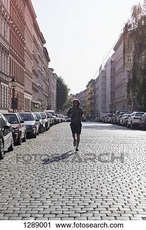 Stock Image - Mid adult man jogging through street. Fotosearch