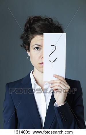 Stock Photography - Portrait of mid adult woman holding paper with question mark, close-up. Fotosearch