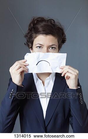 Stock Photography - Portrait of mid adult woman holding paper with frown, close-up. Fotosearch