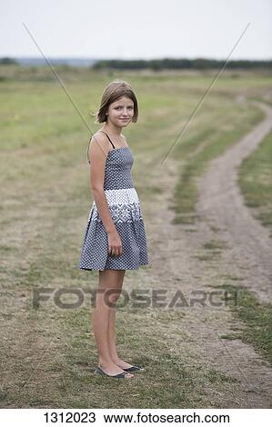 Stock Image - Portrait of teenage girl standing near dirt track. Fotosearch