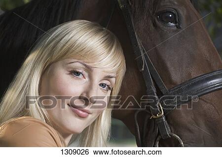 Stock Photograph - Portrait of young woman with horse, smiling. Fotosearch