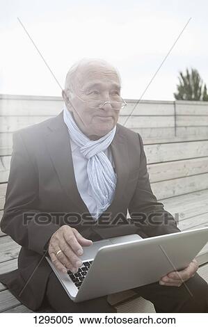Senior man holding laptop, looking away View Large Photo Image Stock Photography - Senior man holding laptop, looking away. Fotosearch