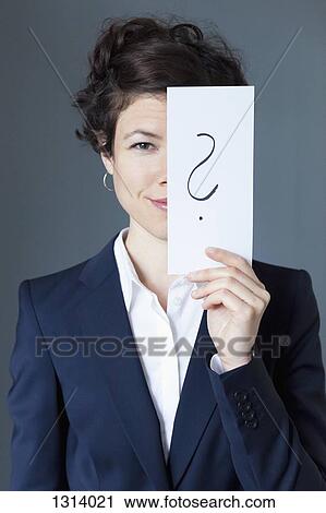 Stock Image - Smiling mid adult woman holding paper with question mark, close-up. Fotosearch