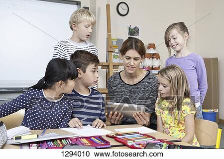 Stock Image - Teacher using digital tablet with students in classroom. Fotosearch
